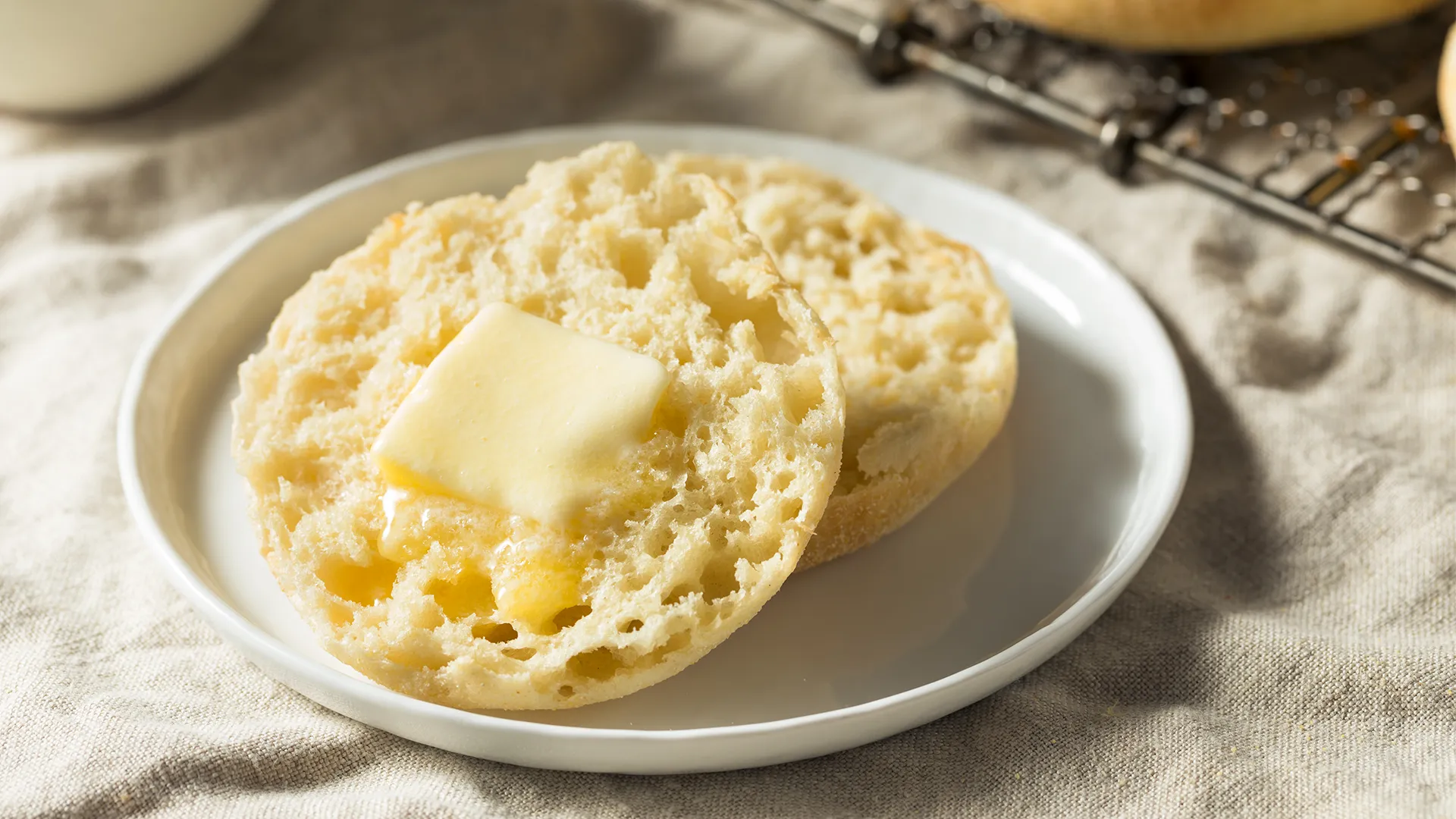 A pack of Hovis Farmhouse Cheddar Muffins is placed on a rustic wooden table, set against a dark grey background.