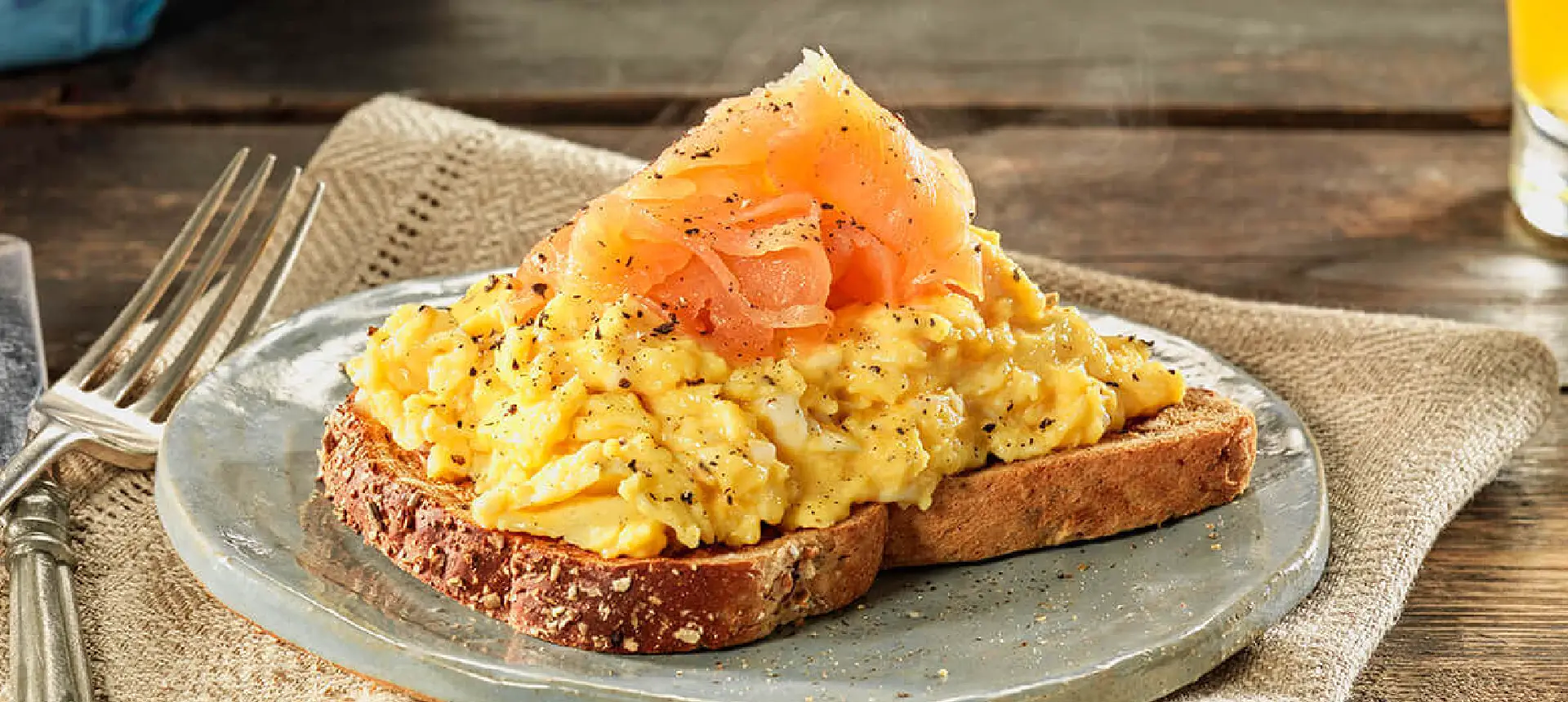 A slice of Hovis Granary Medium Sliced, topped with scrambled eggs, slices of smoked salmon, and a sprinkle of black pepper.