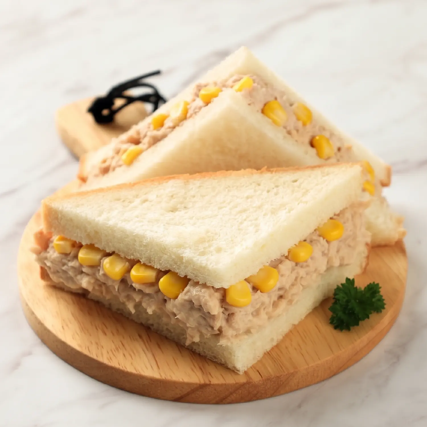 Two halves of a tuna mayo and sweetcorn sandwich on white bread, stacked on a wooden board.