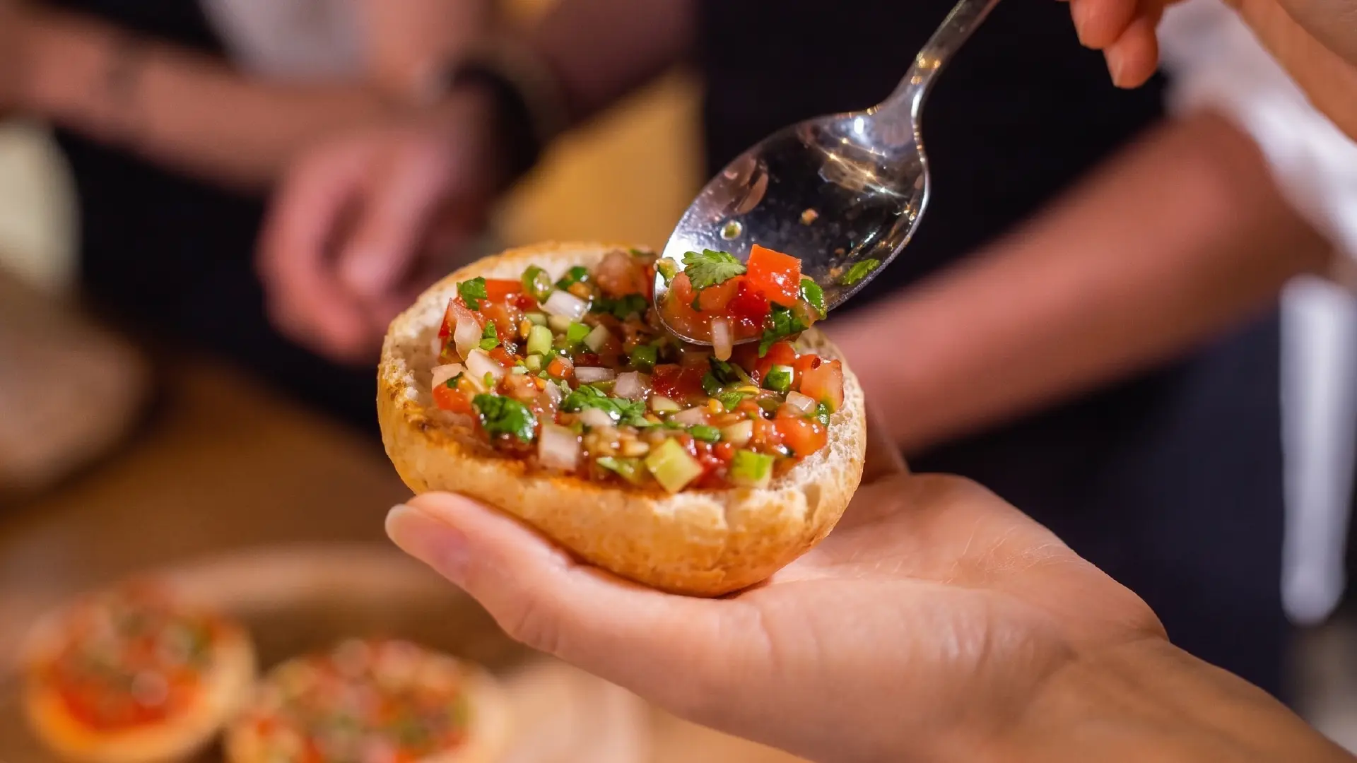 A spoon adding fresh tomato and onion salsa to a toasted Hovis® 4 Premium Burger Bun for a flavourful BBQ burger.