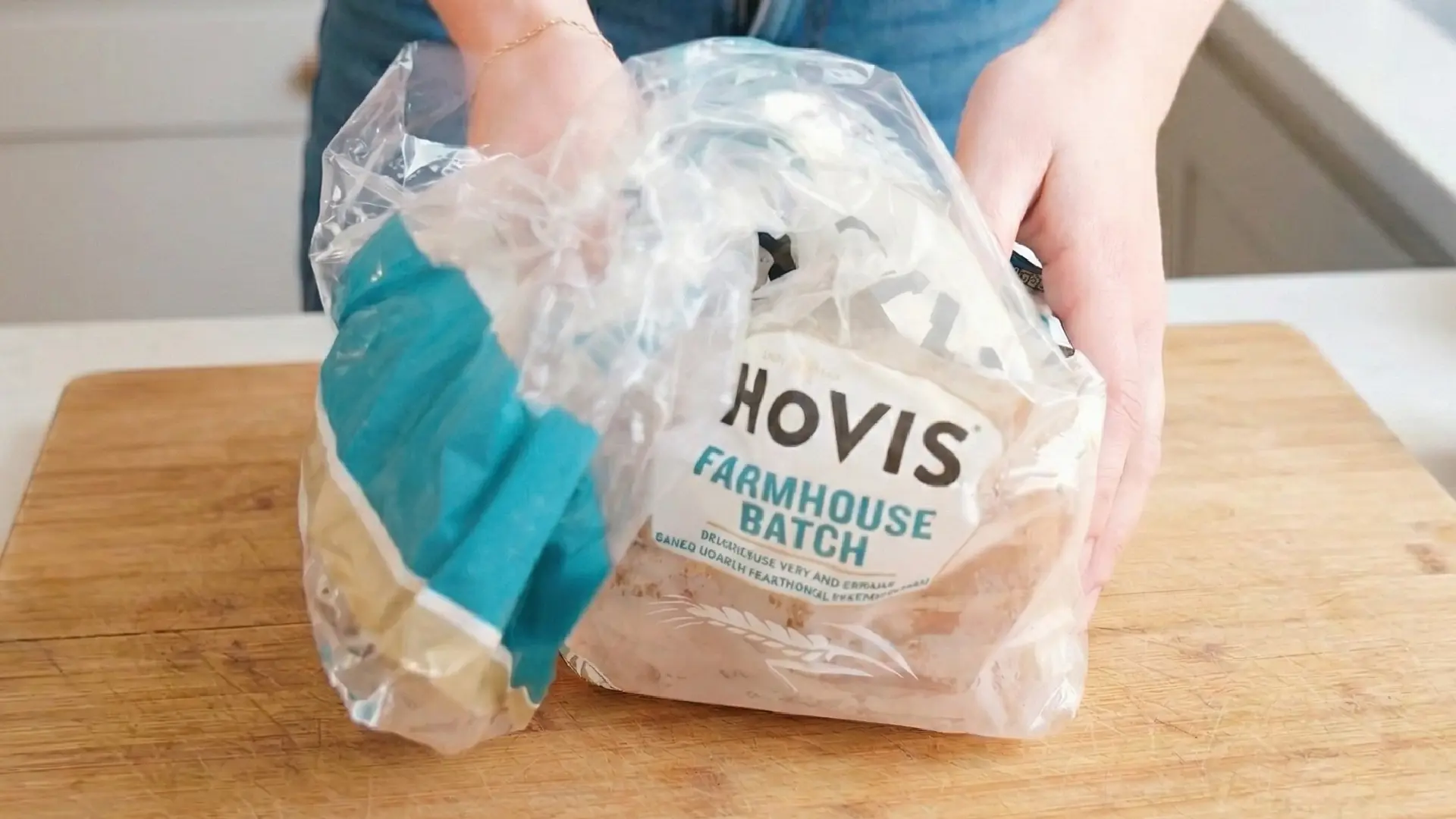 Hands opening a loaf of Hovis Farmhouse Batch bread on a wooden cutting board in a bright, modern kitchen.