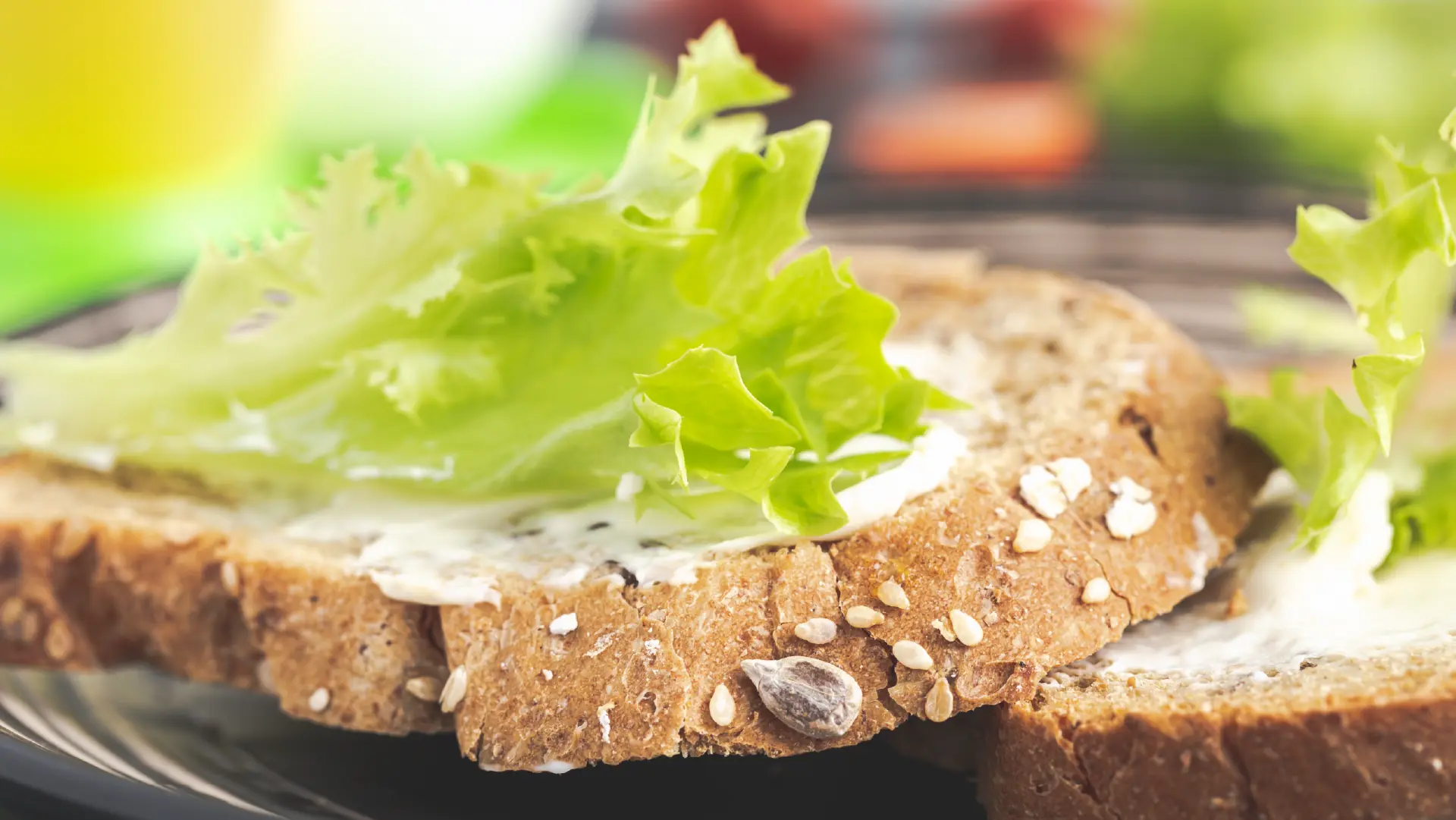 Close-up of seeded granary bread slices spread with butter or mayo and topped with fresh, crisp green lettuce leaves.