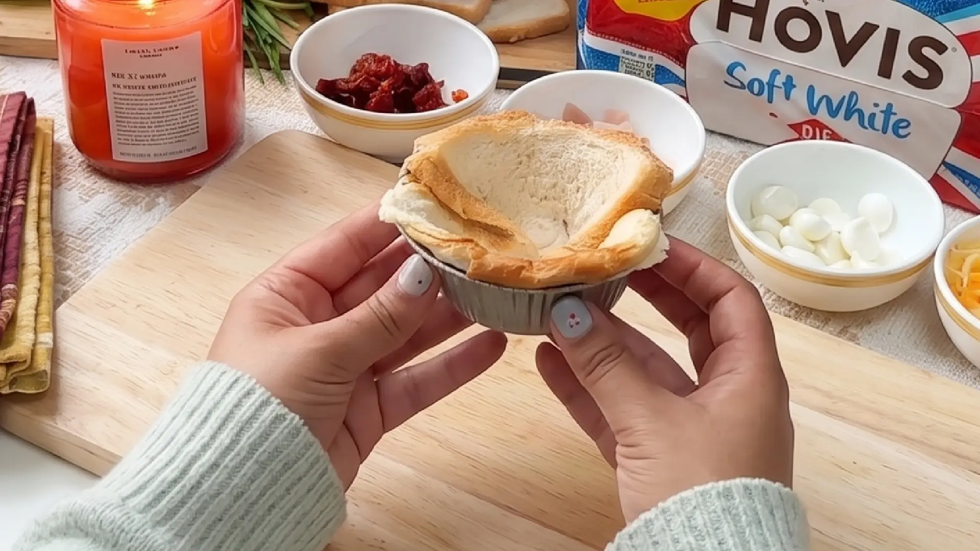 Hands pressing a slice of flattened white bread into a small metal tin to create a pastry cup for baking.