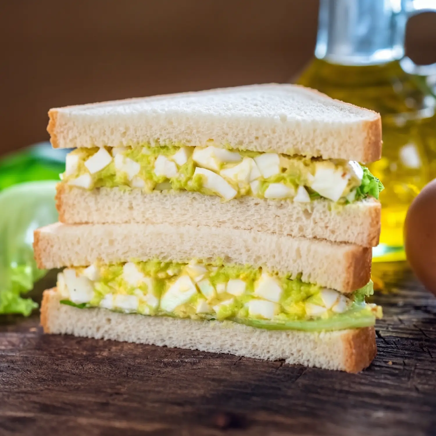 Two halves of an avocado egg sandwich stacked on white bread, showing a creamy green and white egg filling.