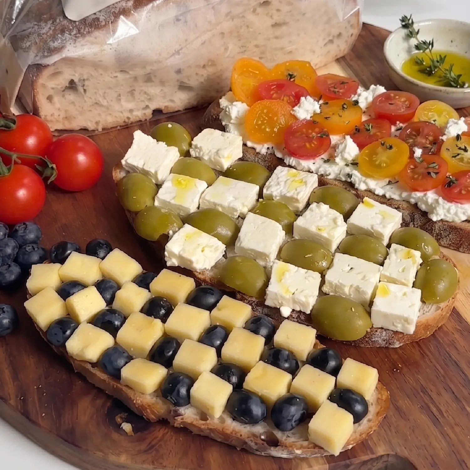 Checkerboard slices of feta, green olives, tomato and cheese cubes with blueberries on sourdough toast.
