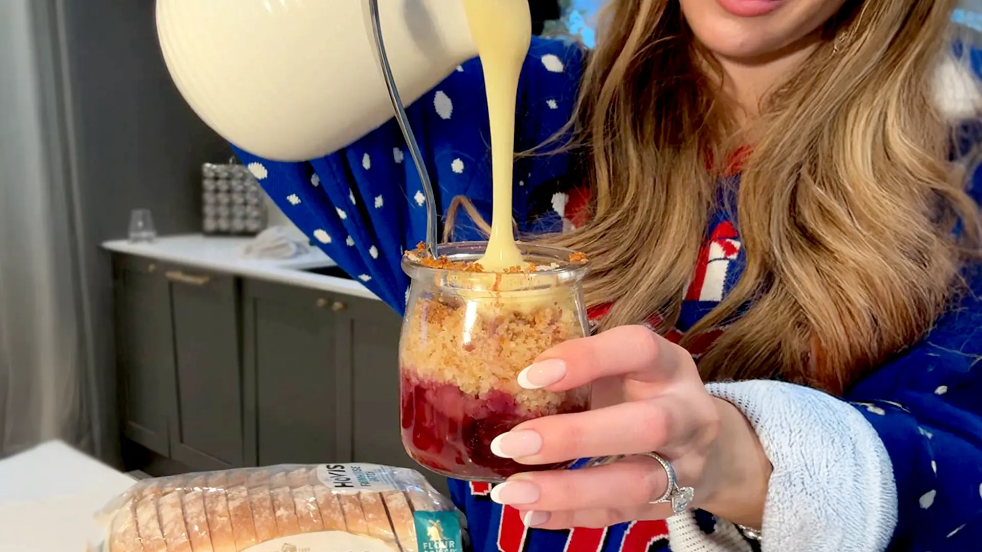 A close-up of hot custard being poured into a jar of golden baked fruit crumble, with a loaf of Hovis® Farmhouse Batch in the background - the bread used to make the buttery crumble topping.