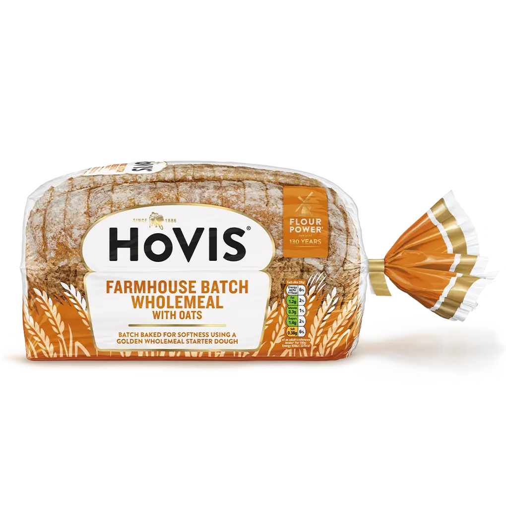 Hovis Farmhouse Batch Wholemeal bread on a white backdrop with a subtle shadow. The packaging is half transparent and orange, decorated with wheats.