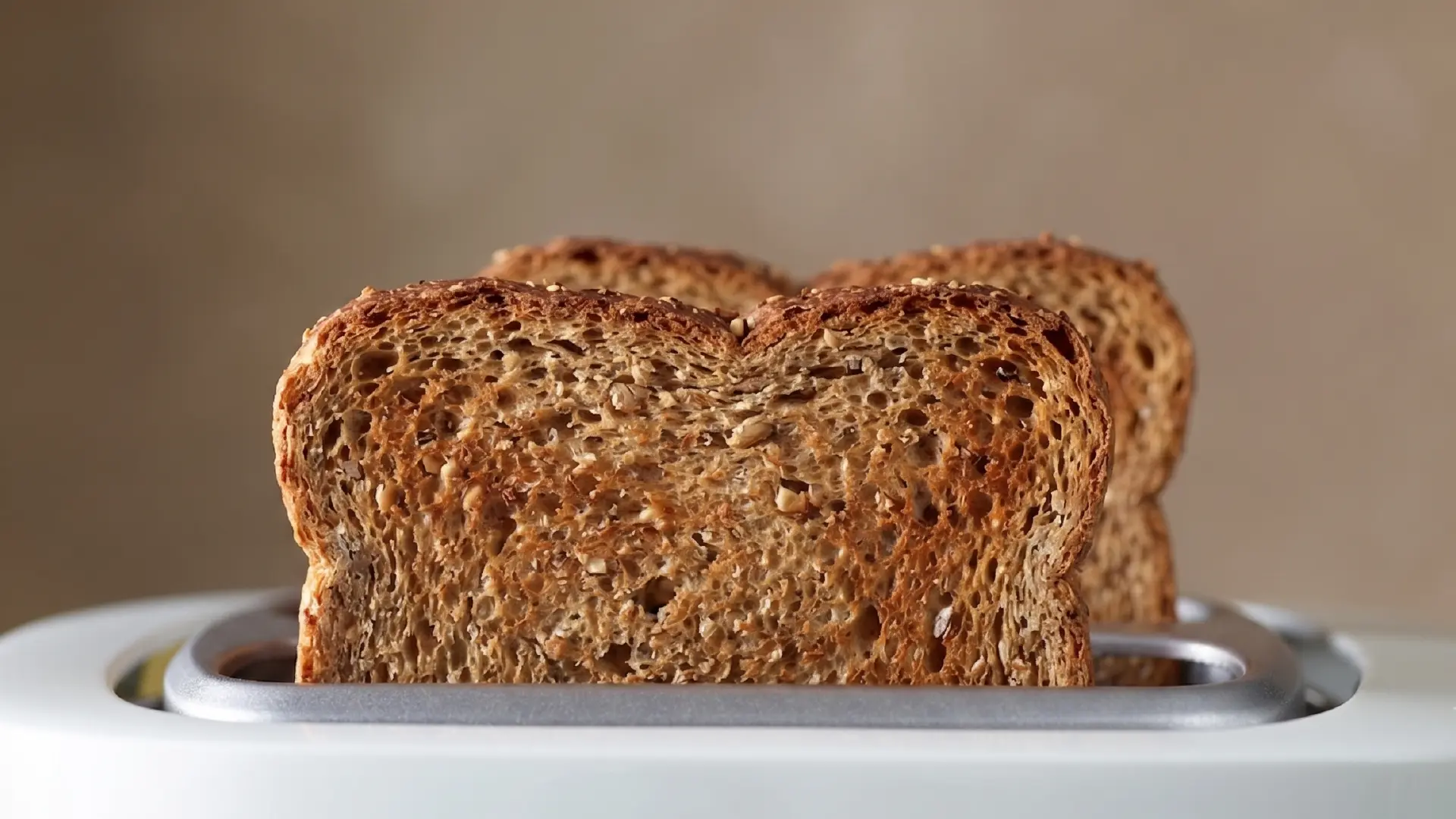 Two slices of golden-brown whole grain toast popping out of a white toaster against a warm, neutral background.
