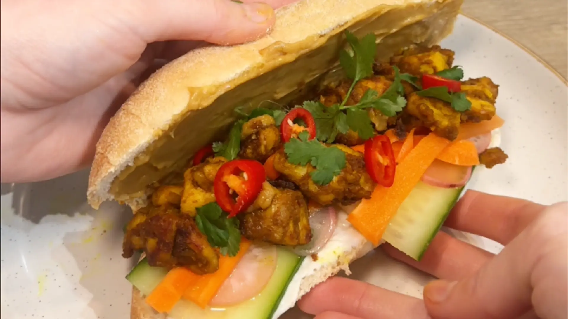 A sub roll cut in half, filled with peanut chicken, chilli and coriander