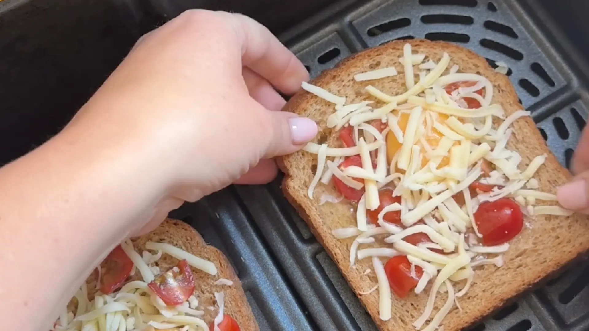 Placing the prepared wholemeal egg-in-a-hole bread slices topped with cheese and tomatoes into an air fryer basket.