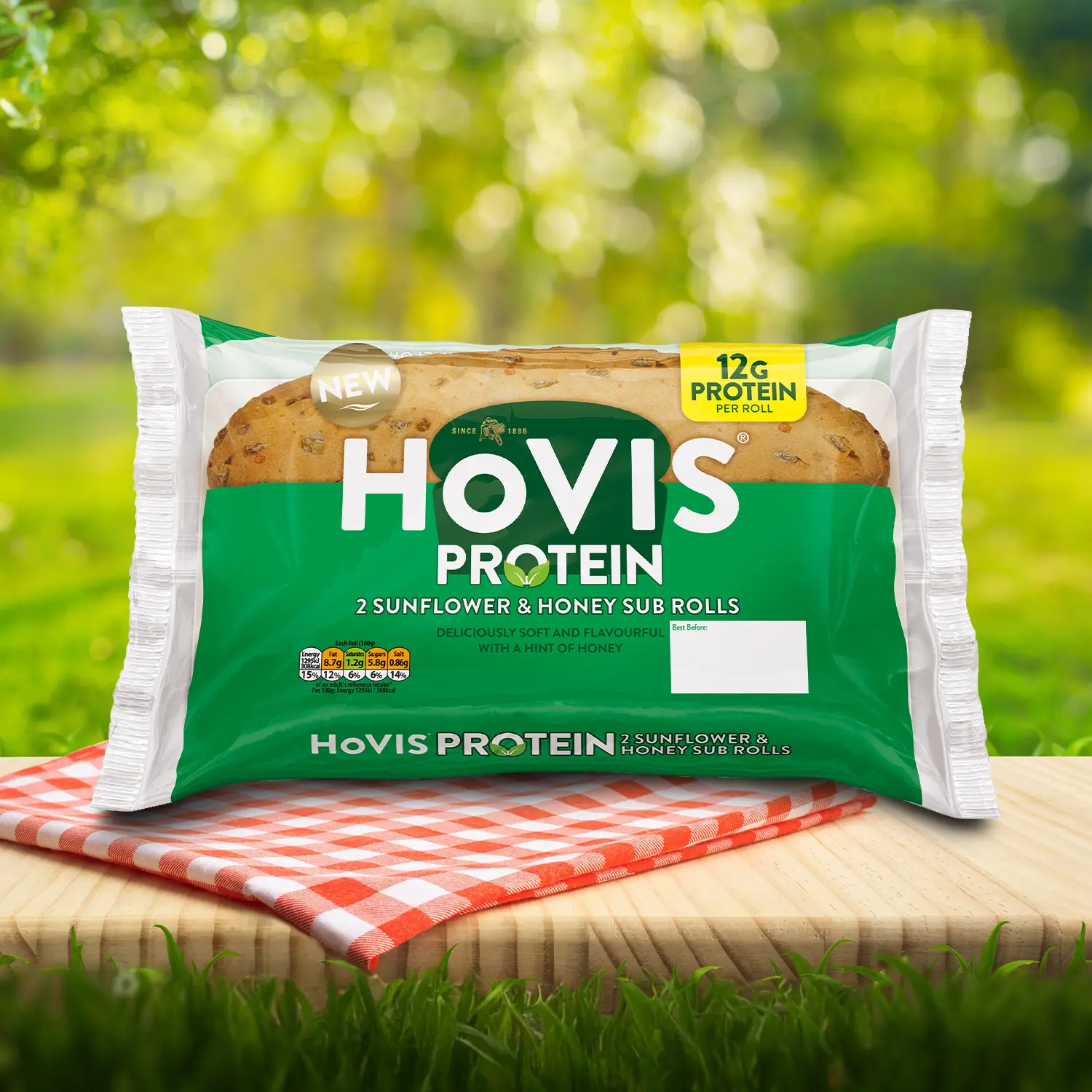 Hovis Protein Sunflower Honey Sub Rolls packaging on a picnic table with a green outdoor background. The pack shows two soft sub rolls with delicious sunflower seed on top “Deliciously soft and flavourful with a hint of honey.” A red gingham cloth adds a picnic feel to the setting.