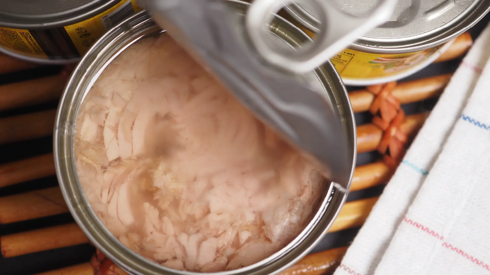 A close-up, overhead view of an open metal tin filled with flaked tuna, with the pull-back lid partially open.
